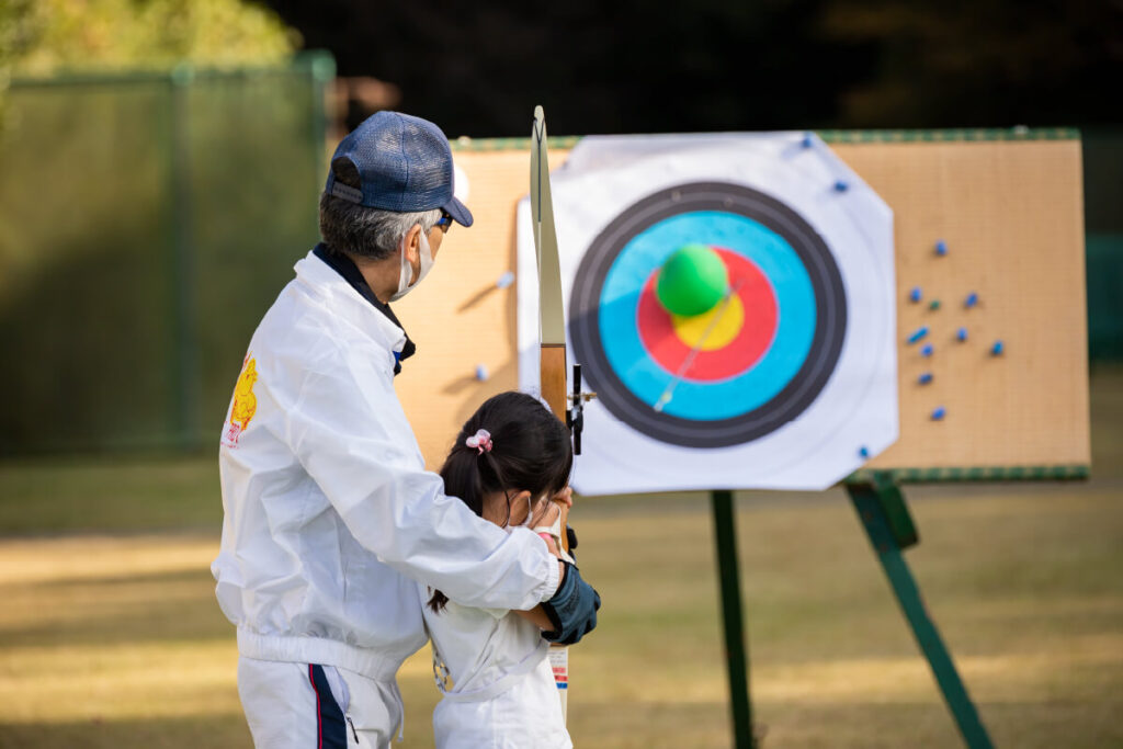 スタッフが子どもにアーチェリーを指導する様子